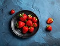 Fresh strawberries on a small black plate against a blue plaster design board. Royalty Free Stock Photo