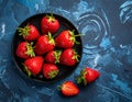 Fresh strawberries on a small black plate against a blue plaster design board. Royalty Free Stock Photo
