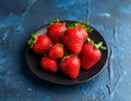 Fresh strawberries on a small black plate against a blue plaster design board. Royalty Free Stock Photo