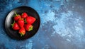 Fresh strawberries on a small black plate against a blue plaster design board. Royalty Free Stock Photo