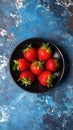 Fresh strawberries on a small black plate against a blue plaster design board. Royalty Free Stock Photo