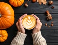 Woman holding tasty pumpkin latte at black wooden table, top view Royalty Free Stock Photo