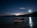 A small wooden boat rests on calm waters under a starry night sky, illuminated by a full moon Royalty Free Stock Photo