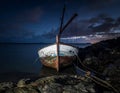 A weathered, wooden boat is moored by rocky shore at night under a starry sky Royalty Free Stock Photo