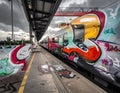 Train station platform with a stationary train covered in colorful graffiti art Royalty Free Stock Photo