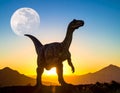 A dinosaur, resembling a theropod, is silhouetted against a vibrant sunset with a full moon in the sky Royalty Free Stock Photo
