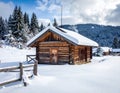 A rustic log cabin sits in a snow-covered landscape. The cabin has a pitched roof blanketed with snow, a wooden door Royalty Free Stock Photo