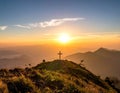 A scenic mountain landscape at sunrise with a prominent wooden cross atop a grassy hill Royalty Free Stock Photo