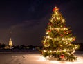 An illuminated Christmas tree adorned with red and gold ornaments and twinkling lights stands on a snowy surface Royalty Free Stock Photo