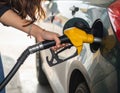 A woman refuels a car at a gas station, holding a yellow fuel nozzle inserted into the car\'s fuel tank Royalty Free Stock Photo