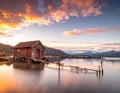 A rustic wooden boathouse on stilts stands over calm water, reflecting a colorful sunset Royalty Free Stock Photo
