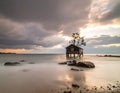 A solitary wooden hut on stilts stands in calm, shallow water, accompanied by a single tree Royalty Free Stock Photo