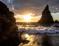 Sunset scene with waves crashing against a rocky shore, featuring a tall, rugged rock formation rising from the sea Royalty Free Stock Photo