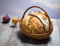 A round loaf of crusty bread is placed in a wicker basket with a handle,resting on a rustic wooden surface Royalty Free Stock Photo