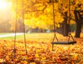 A swing hangs on metal chains in a park covered with vibrant orange and yellow autumn leaves Royalty Free Stock Photo