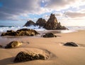 Golden sandy beach with textured rocks leading to large, jagged rock formations in the surf Royalty Free Stock Photo