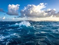 Waves crash energetically in a deep blue ocean under a bright sky with dramatic cloud formations Royalty Free Stock Photo