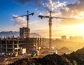 Construction site at sunset featuring two towering cranes and partially built multi-story buildings Royalty Free Stock Photo