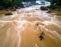 Rushing river with muddy brown water coursing through a landscape of large rocks and dense greenery Royalty Free Stock Photo