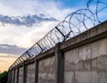 A concrete wall topped with coiled barbed wire under a partially cloudy sky Royalty Free Stock Photo