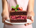 Woman holding plate with slice of chocolate sponge berry cake on grey background Royalty Free Stock Photo