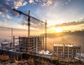 Construction site at sunrise with two tall cranes towering over partially constructed multi-story buildings Royalty Free Stock Photo