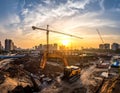 Urban construction site at sunset featuring a prominent yellow excavator and a towering crane Royalty Free Stock Photo