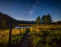 A serene night scene in a mountainous area featuring a dirt path bordered by wooden fence Royalty Free Stock Photo