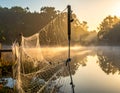 Misty sunrise over a serene lake, with a close-up view of a delicate spider web stretched across a rope fence Royalty Free Stock Photo
