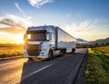 A semi-truck with a lengthy trailer travels along a paved road during sunset Royalty Free Stock Photo