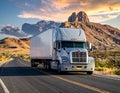 A large silver semi-truck travels along an asphalt highway in a desert landscape Royalty Free Stock Photo
