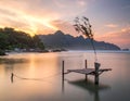 Tranquil beach scene at sunrise. A small wooden pier juts gently above calm, reflective water Royalty Free Stock Photo