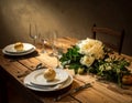 A rustic wooden table set for a meal, featuring two place settings with white plates and bread rolls on each Royalty Free Stock Photo