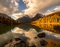 Golden autumn trees surround a tranquil alpine lake, reflecting the dramatic peaks of snow-capped mountains Royalty Free Stock Photo