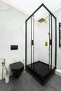 Modern Luxury Bathroom Interior with Black Glass Shower Cabin, Matte Gold Rain Shower, Black Toilet, Marble Tile Walls Royalty Free Stock Photo