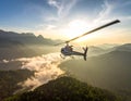 A helicopter flies over a mountainous landscape at sunset, casting soft shadows over the forested hills below Royalty Free Stock Photo