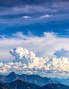 A dramatic sky with large, fluffy cumulus clouds dominates the scene above a range of jagged, rocky mountains Royalty Free Stock Photo