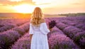 Blonde woman poses in lavender field at sunset. Happy woman in white dress holds lave Royalty Free Stock Photo