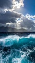 Turquoise ocean waves crash forcefully under a dramatic cloudy sky, with sunbeams piercing through the clouds Royalty Free Stock Photo