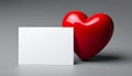 A shiny, red heart-shaped object is positioned next to a blank white card Royalty Free Stock Photo
