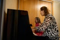 Authentic side portrait of a music teacher with the pupil, sitting at vintage wooden piano at home, enjoying a music