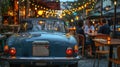 Blue car parked near a restaurant with outdoor seating and string lights. Royalty Free Stock Photo