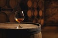 cognac in snifter glass on old wooden barrel in cool and dark cellar