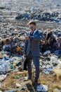 Businessman looking at watch, checking time standing on landfill, large pile of waste. Consumerism versus pollution Royalty Free Stock Photo