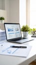 Laptop displaying financial charts and documents on a white desk, bright office setting. Royalty Free Stock Photo