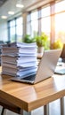 Laptop and large stack of paperwork on a wooden desk in a bright office. Royalty Free Stock Photo