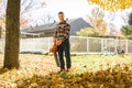 A Man cleaning fallen leaves using a leaf blower on the lawn. Royalty Free Stock Photo