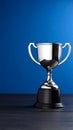 Shiny silver trophy cup on dark wooden surface against a blue background Royalty Free Stock Photo