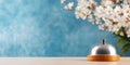 Silver desk bell on a wooden base placed on a light surface with cherry blossoms and a vibrant blue background, evoking Royalty Free Stock Photo