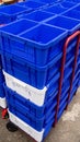 Stack of vibrant blue and white plastic storage crates on a red hand truck outdoors Royalty Free Stock Photo